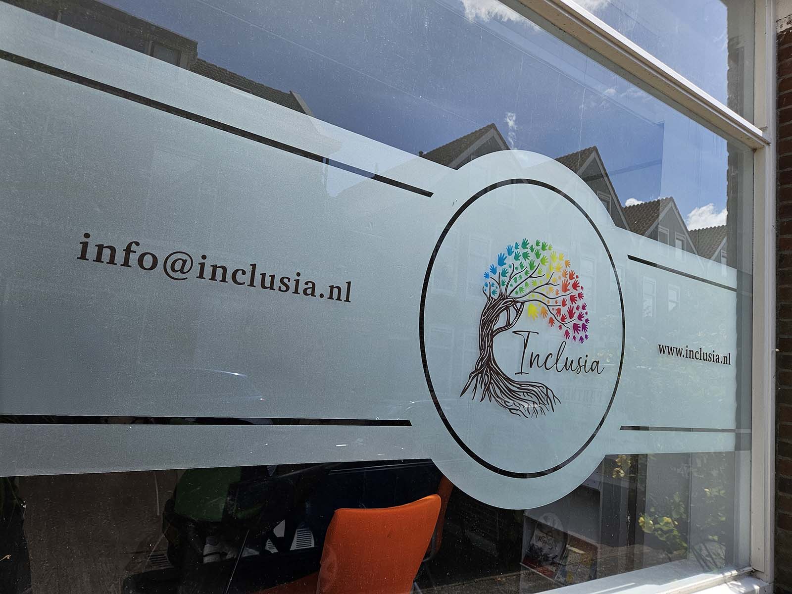 Professioneel gemonteerde matglasfolie met full-color logo en contourgesneden details voor Inclusia – een stijlvolle combinatie van privacy en herkenbaarheid.