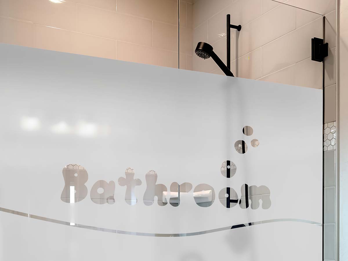 Zelfklevende matglasfolie op een glazen douchewand met de uitgesneden tekst "Bathroom".