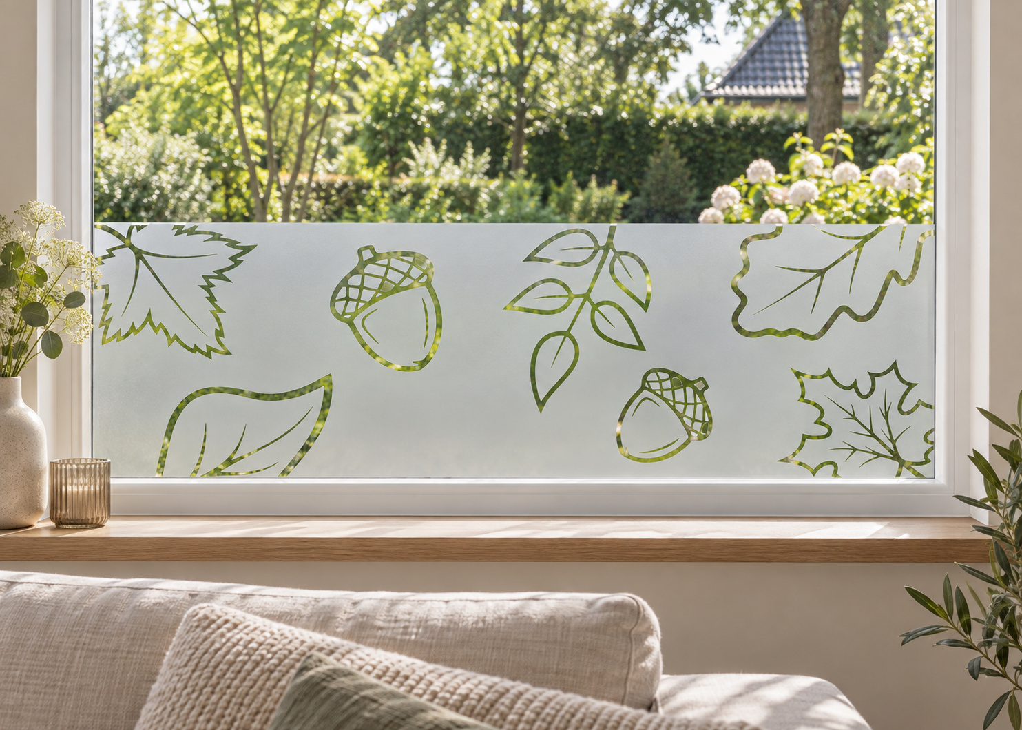 Raamfolie bladeren en eikeltjes (RFH104) als horizontale raamfolie boven de vensterbank in een woonkamerraam, met matte folie en doorkijk naar de tuin.