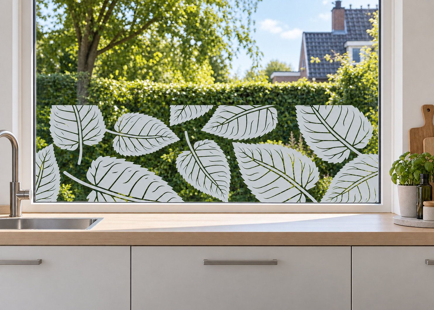 Raamfolie bladpatroon (RFH103) als horizontale raamfolie boven het aanrecht in een keukenraam, met matte folie en doorkijk naar de tuin.