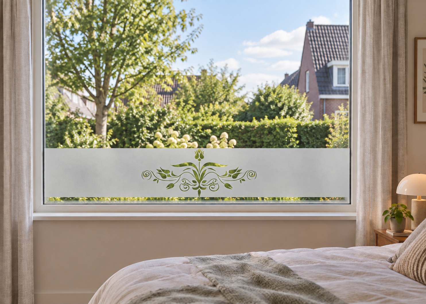Raamfolie in klassieke stijl met bloem ornament (RFH015) als horizontale raamfolie boven de vensterbank in een slaapkamerraam, met matte folie en doorkijk naar de tuin.