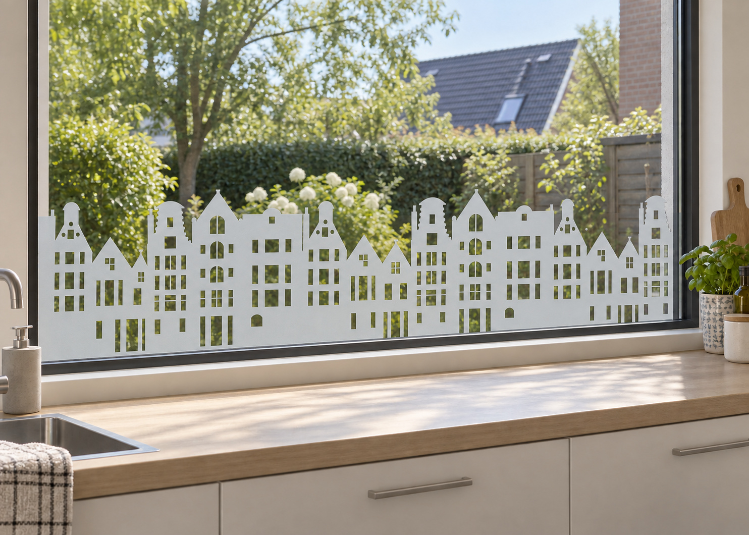 Raamfolie met huisjes (RFH024) als horizontale raamfolie boven het aanrecht in een keukenraam, met matte folie en doorkijk naar de tuin.