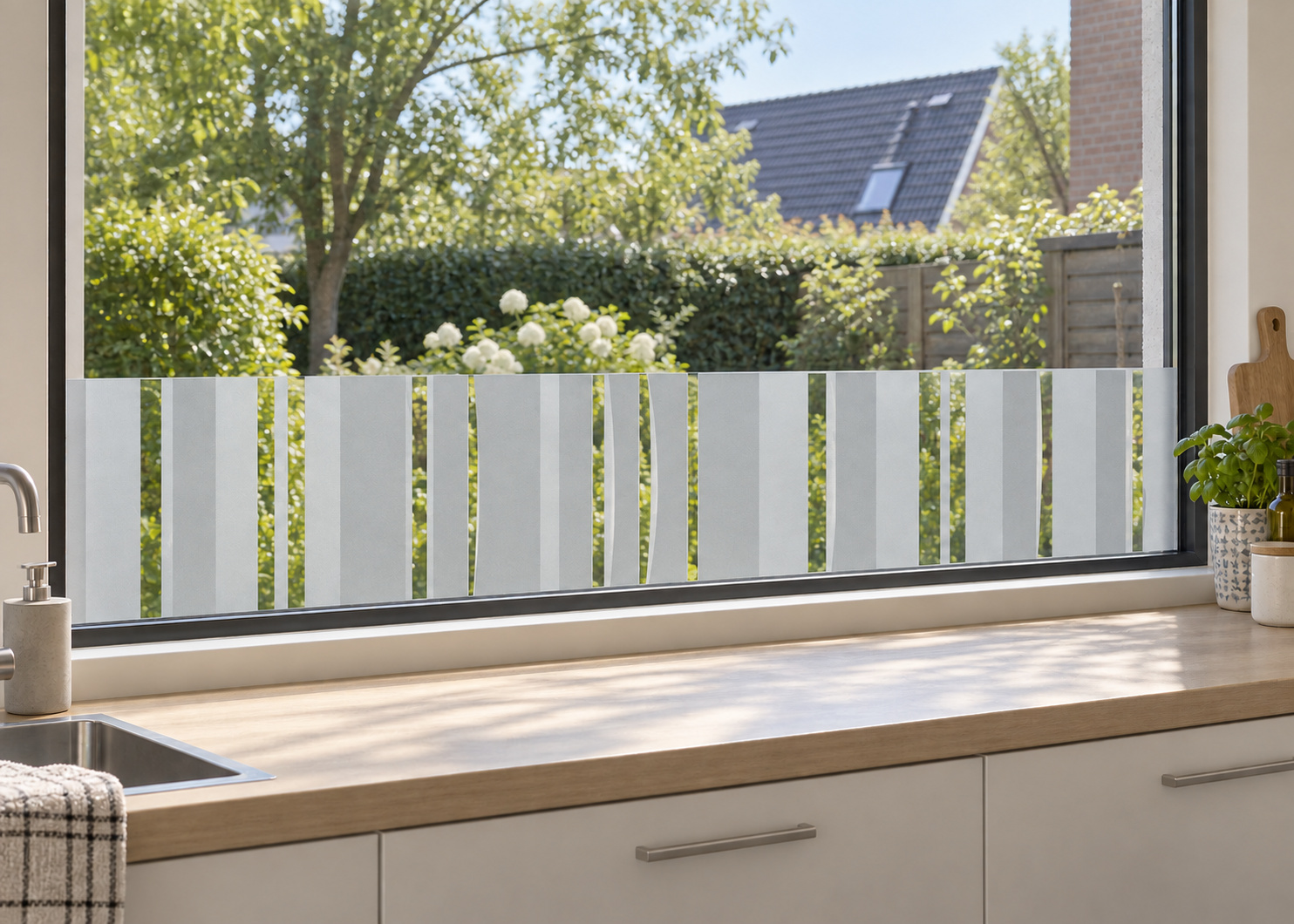 Raamfolie met veel strepen (RFH070) als horizontale raamfolie boven het aanrecht in een keukenraam, met matte folie en doorkijk naar de tuin.