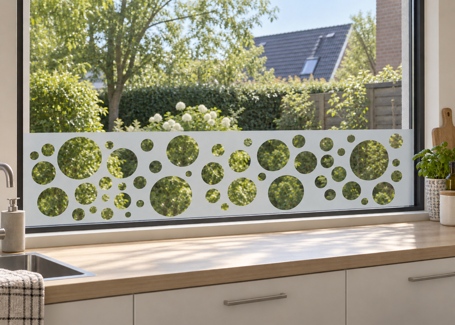 Raamfolie retro cirkels (RFH009) als horizontale raamfolie boven het aanrecht in een keukenraam, met matte folie en doorkijk naar de tuin.