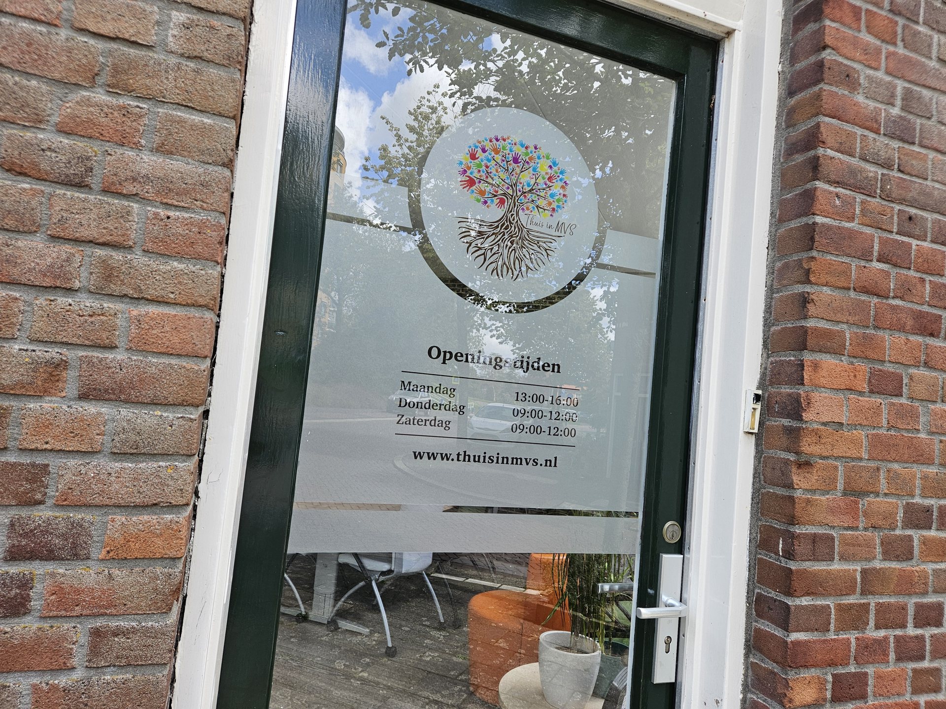 Bedrukte matglasfolie met logo op een entreedeur Glazen entreedeur met matglasfolie, een gekleurd logo en uitgesneden ronde elementen.